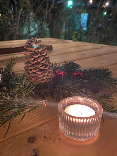 Windlicht mit Kerze, Tannenzweige und Zapfen auf einem Holztisch