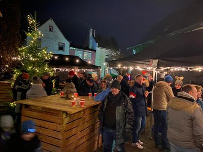 Gäste am Weihnachtsbaum und an der Holztheke beim Winterzauber am Abend